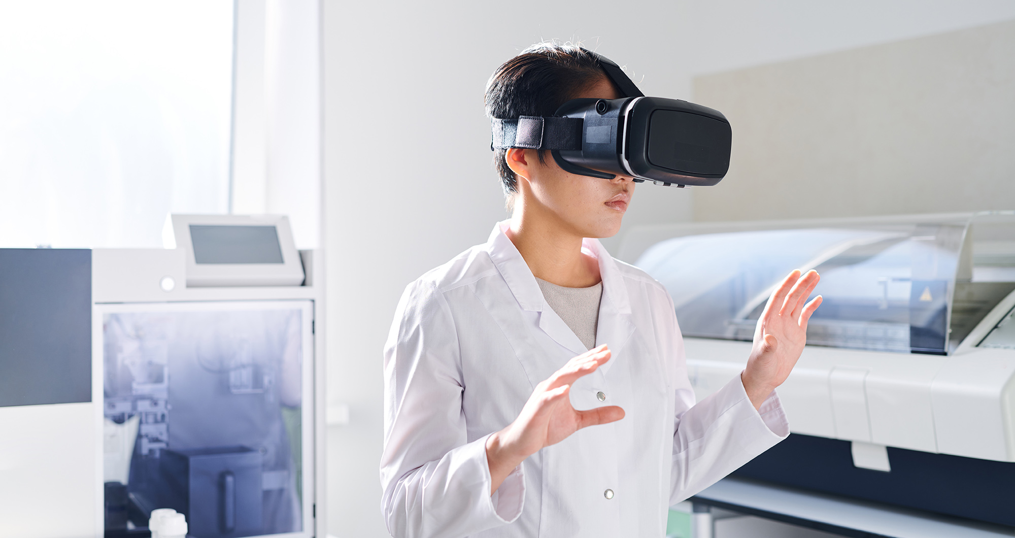 Young Asian laboratory scientist with short hair standing in modern laboratory and using virtual reality simulator while watching educational video